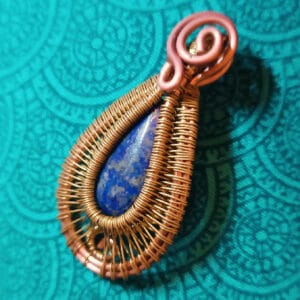 Ce collier met en avant un lapis lazuli taillé en goutte enlacé de cuivre et de laiton sans perçage ni colle. Le cordon est réalisé dans un lacet tissé brun. Ce collier peut se porter dans les deux sens.